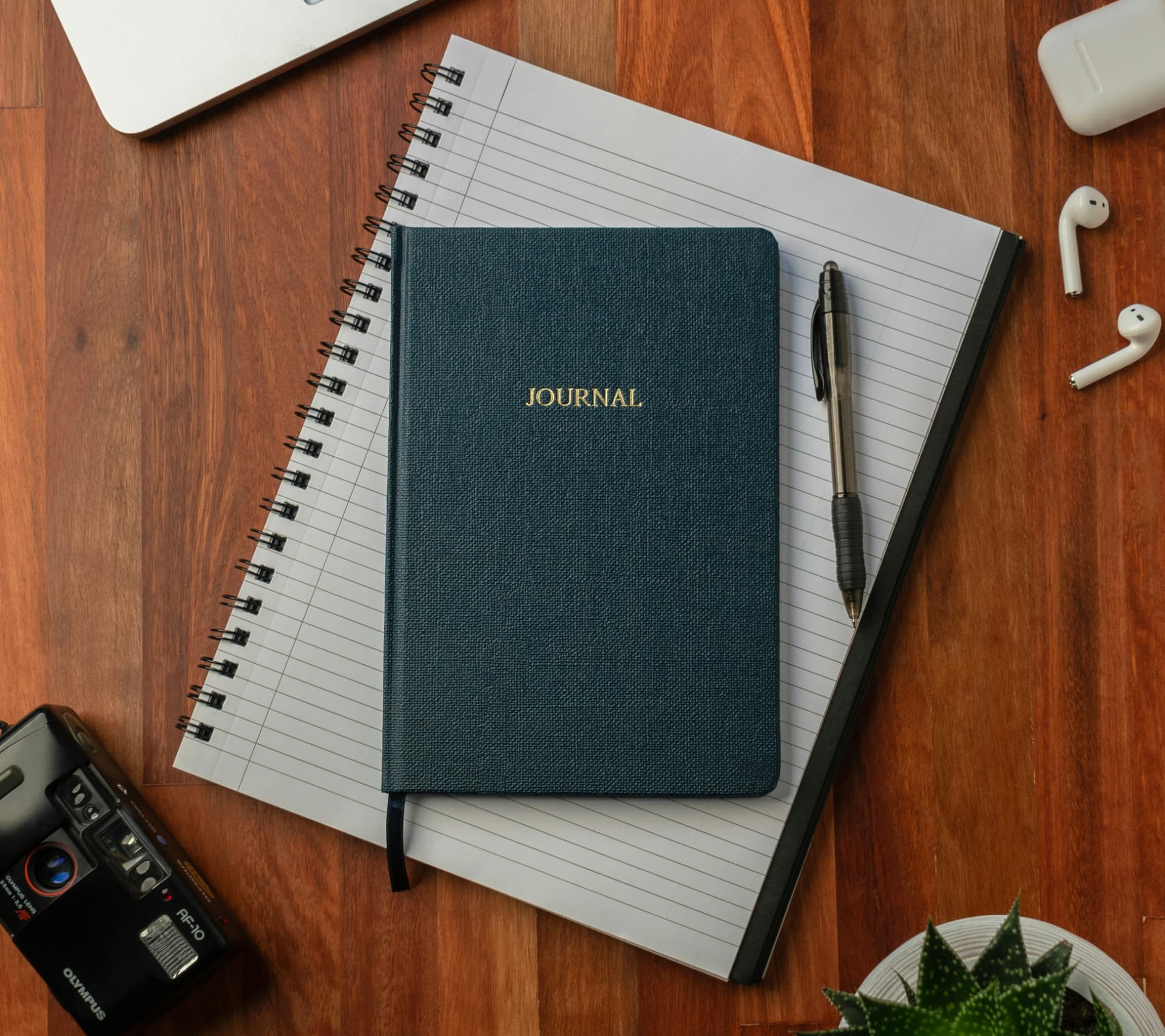 A journal, notebook, and pen on a wooden desk